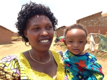 A woman in a yellow dress holding a baby in a bright blue shirt. Both are smiling. 